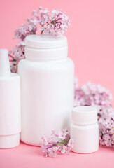Fototapeta na wymiar Face and body skin care. A set of cosmetic creams and balms in white tubes and cans on a coral background with sprigs of lilac flowers. Spa treatments for home care. Home rejuvenation and moisturizing