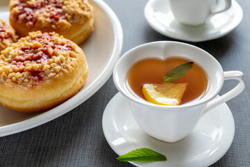 Sweet round donuts on plates and small cups with mint tea on the table. Tasty breakfast.