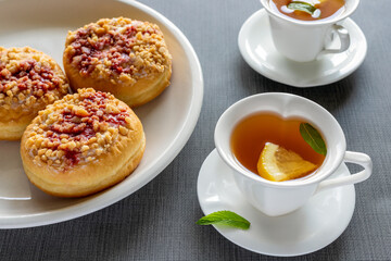 Sweet donuts on plates and cups with mint tea on grey table. Tasty breakfast.