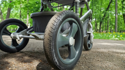 Wheels of baby stroller go round and baby carriage rides back and forth in green park. Wheels move on pavement blurred on background closeup