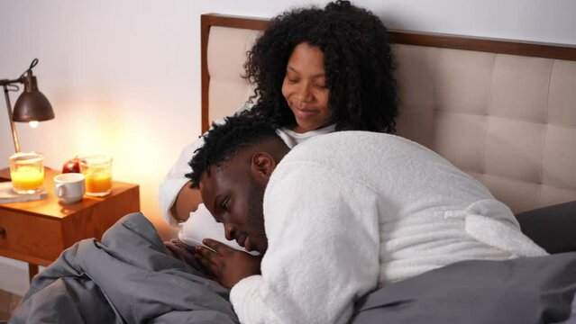 Happy Young African American Father Listening Talking To Pregnant Belly Of Smiling Mother As Cute Toddler Running In Bedroom. Smiling Handsome Man And Beautiful Woman Lying In Bed Resting