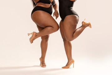 Photo of real, superb, plus size, dark skinned two womens bodies. Concept of body acceptance, body positivity. Legs in high heels. - obrazy, fototapety, plakaty