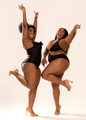 Full photo of superb plus size dark skinned two women in black fashionable swimwears, laughing and...