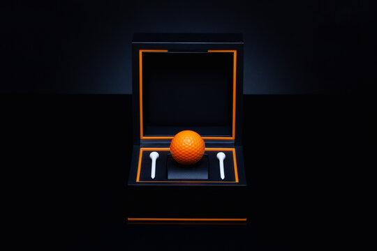 Black box with orange golf ball and white golf tees.