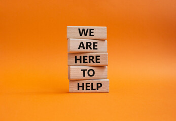 We are here to help symbol. Concept words we are here to help on wooden blocks. Beautiful orange background. Business and we are here to help concept. Copy space.