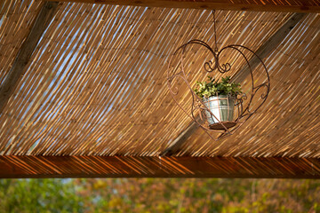 Flower decoration under sun protection roof made of bamboo. Decorated with elaborately forged frame in the shape of a heart.