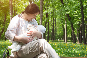 Naklejka na ściany i meble Mother breastfeeds little baby in park outdoors, copyspace