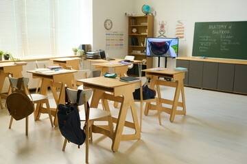 Spacious classroom of biology or anatomy with several wooden desks with chairs in the center in front of blackboard with notes