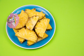 Pineapple slices with an umbrella on a blue plate on a pastel green background