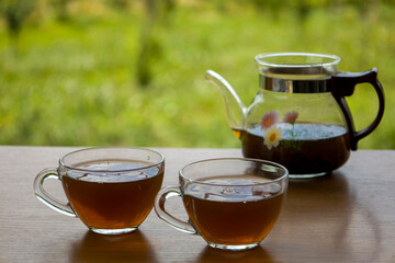 Teapot with a transparent cup of tea in nature