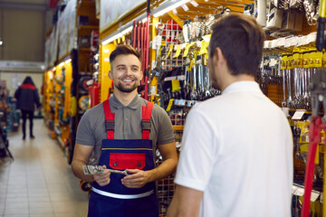Obraz na płótnie Canvas Friendly shop assistant at DIY retail store helping customer choose tools and equipment. Happy smiling salesman helping young man who is buying wrenches and other tools for home repairs
