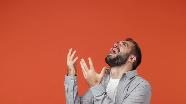 Angry puzzled dolour young brunet man 20s years old wears blue shirt looking up scream ask why shake hands close ears with hands not want to listen isolated on plain orange background studio portrait