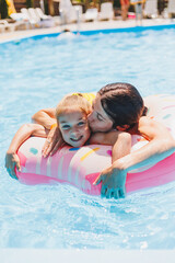 Mother and daughter with an air mattress swim in the pool near the hotel. Family summer vacation concept