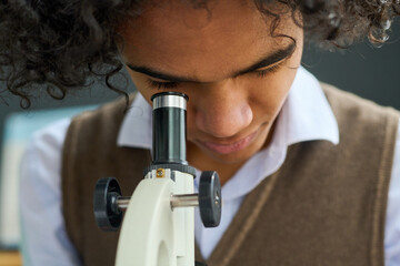 Close-up of teenage guy studying chemical or biological substance in microscope at lesson of...