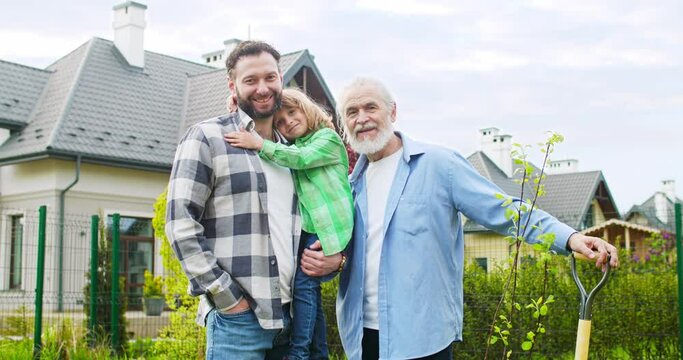 Portrait of happy three generations of family. Man with old father and cute little son in garden after planting work. Cheerful grandfather with son and grandson at summertime house.