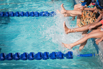 Group of diverse multiethnic children kicking splashing water at poolside of swimming class in...