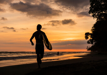 Man carrying surfboard on beach at sunset