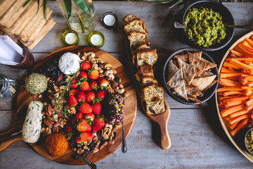 Vintage wood table with delicious and colorful vegetarian/vegan catering with carrot, hummus, avocado, toasts and olive, vegan gourmet cheese,  strawberries, nuts and crackers