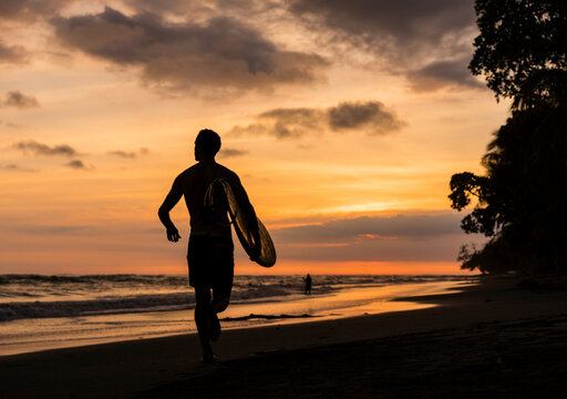 Man carrying surfboard on beach at sunset