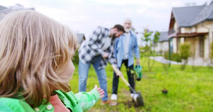 POV from small cute boy taking video in garden and showing father with grandfather planting trees in garden. Videochat. Summer work at village house. Outdoor. Videochatting.