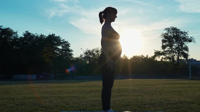 Silhouette of a pregnant woman doing stretching and yoga at sunset. Beautiful pregnant woman practicing yoga in nature. Yoga at the sports stadium, sports lifestyle