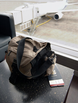 Travel bag and passport on table at airport and aeroplane parked outside window
