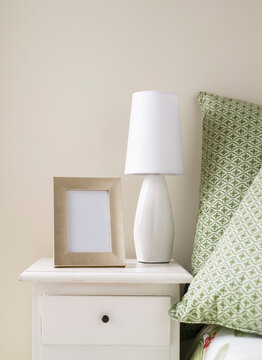 Blank picture frame and lamp on bedside table in the bedroom