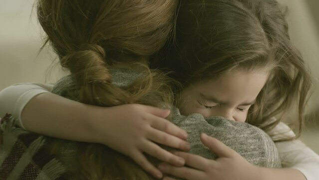 Daughter rushes into mother's arms at home and gives her a big hug . Happy cute little kid girl hugging parent mother with eyes closed . Adorable small child daughter embrace mum .  close up view