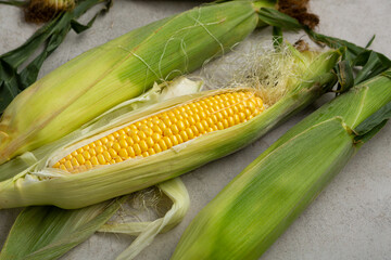 Yellow corn cob with green husk food on light surface