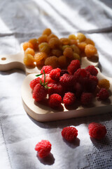 Two handfuls of fresh red and yellow raspberry on white wooden kitchen boards.