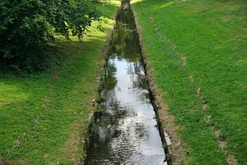 Obraz premium Fluss mit Spiegelung im Park mit grünen Wiesen und Bäumen bei Sonne am Nachmittag im Frühling