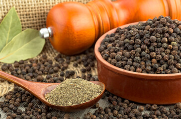 Wooden pepper mill, laurel leaves, black peppercorns and ground black pepper on old wooden table.