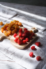 Two handfuls of fresh red and yellow raspberry on white wooden kitchen boards with copy space.