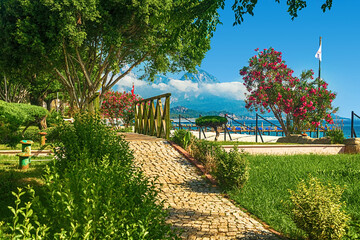 View of the path and the bridge in a green garden with green trees along the embankment in Kemer, Turkey.