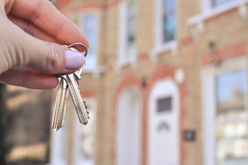 Woman's hand with metal keys on blurred background with house. High quality photo
