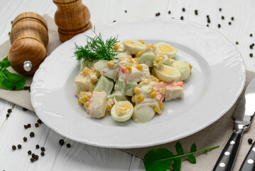 Salad with crab sticks, sweet corn, cucumber, eggs and mayonnaise on light table.