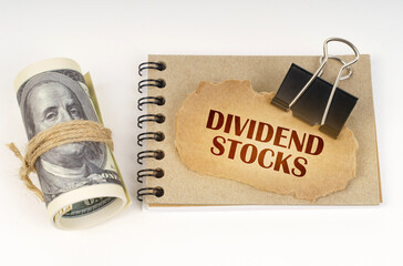 On a white surface are twisted dollars, a notebook and a cardboard sign with the inscription -...
