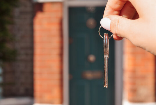 Woman's hand with metal keys on blurred background with house. High quality photo