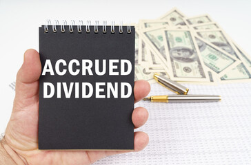 In the man's hand is a notepad with the inscription - ACCRUED DIVIDEND, in the background a pen and...