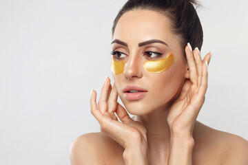 Beautiful woman with gold patches for eyes on a grey background. Patch under eyes. Collagen mask. Portrait of female, facial treatmen