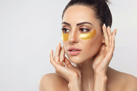 Beautiful woman with gold patches for eyes on a grey background. Patch under eyes. Collagen mask. Portrait of female, facial treatmen