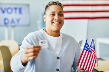 Waist up portrait of smiling person holding voting sticker and American flag on election day