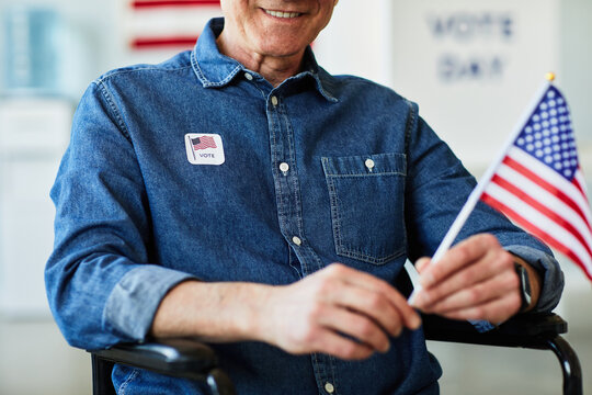 Cropped shot of man in wheelchair holding American flag in voting station, copy space