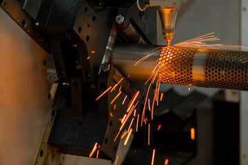 CNC laser cutting machine working with cylindrical metal workpiece with many sparks at factory,...