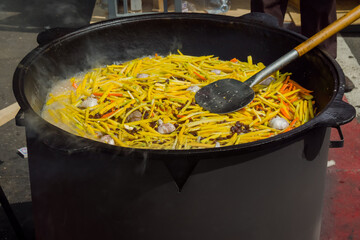 Process of cooking potato, carrots slices, garlic for Uzbekistan pilaf in huge cauldron at summer outdoor food market. Oriental cuisine, cookery, gastronomy and street food concept