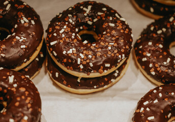 Donuts with multicolored sprinkles, isolated on a light background. Top view of donuts with chocolate glaze. Round chocolate donuts on the counter in the bakery selective focus. Street food desserts.	