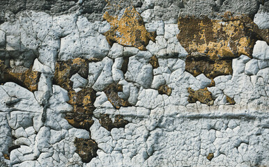 Swollen peeling paint on the old texture of the wall background. The rough cracked white paint on the walls was peeling off. The yellow cracked paint has damaged the rough texture of the concrete.	