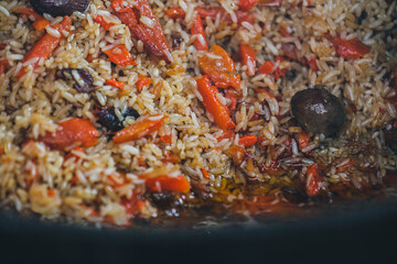 Cooking rice, pilaf in a cauldron. The concept of cooking street food. Juicy beef pilaf is cooked in a cauldron on the street in close-up. Red and yellow rice. Close up of a pile of rice. 