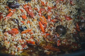 Cooking rice, pilaf in a cauldron. The concept of cooking street food. Juicy beef pilaf is cooked in a cauldron on the street in close-up. Red and yellow rice. Close up of a pile of rice. 