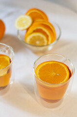 Citrus tea in a glass mug with a double bottom against the background of a teapot and oranges